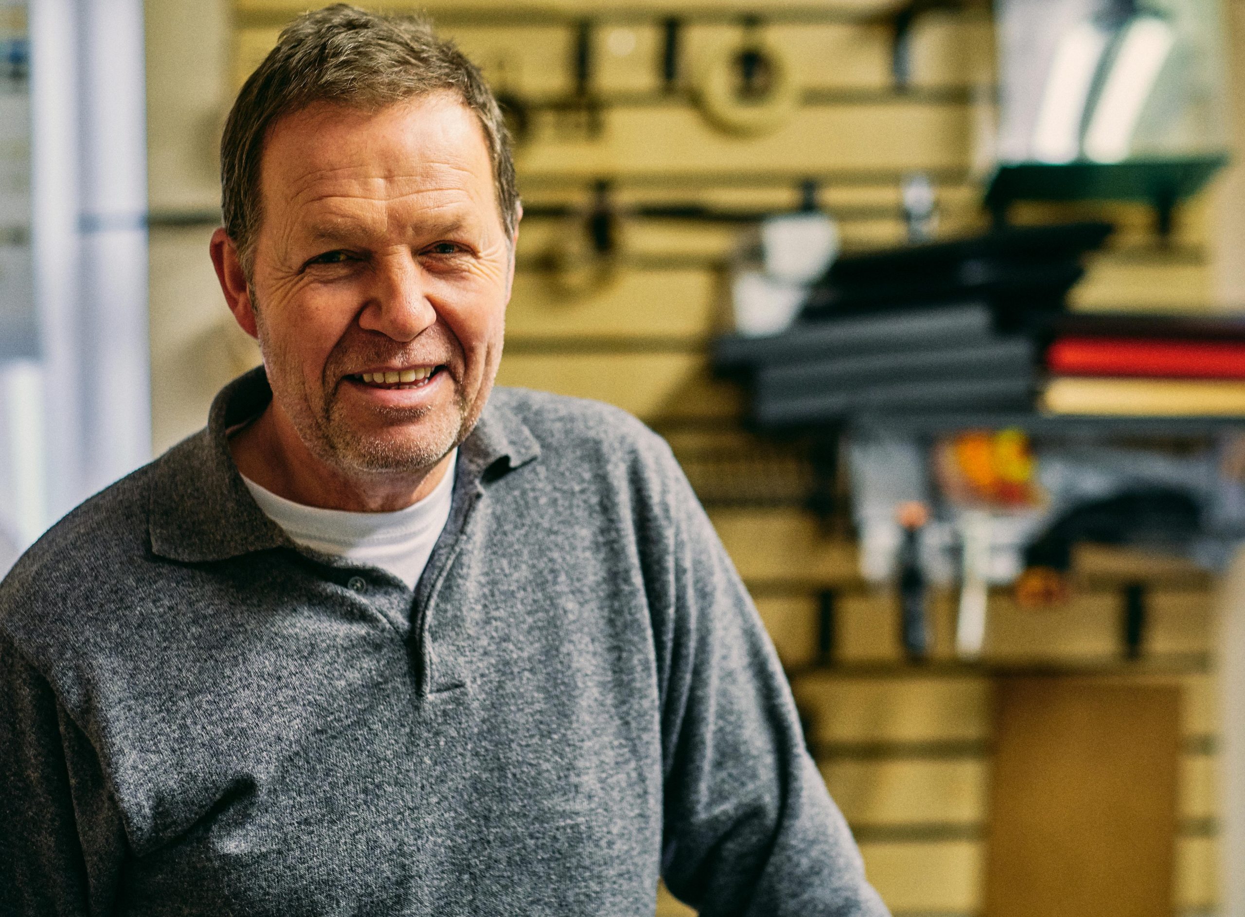 A happy caucasian man in a casual gray shirt smiling warmly at the camera indoors.